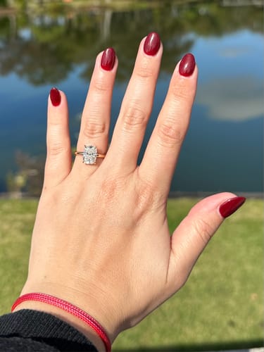 Customer's hand wearing the Plunge Hidden Halo ring with a cushion cut diamond on a gold band outdoors.