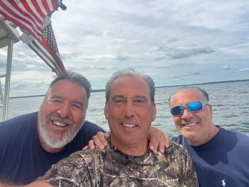 Reviewer with two friends smiling on a boat with a flag flying in the background over the water.