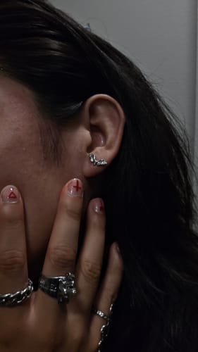 Close-up of a reviewer's ear showing the detailed Deathwing Stud Earring, with their hand and rings visible nearby.