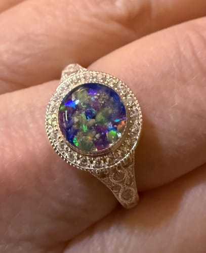 Customer wearing their Bedazzled Filigree Cremation Ring. The round center features colorful crushed opal in a decorative silver band.