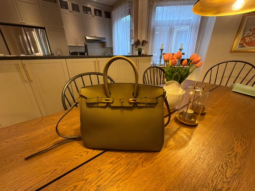 Reviewer's structured, olive-green Warkin Bag with gold hardware, shown on a wooden table in their home.