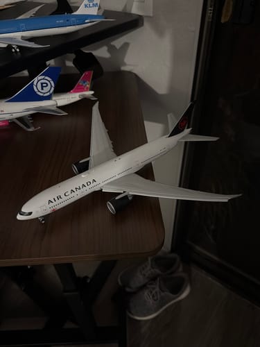 Customer's GEMINI200 Air Canada 777 model airplane displayed on a dark wooden table with other models in the background.