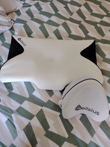 Photo d'une cliente du combo oreiller cervical et coussin pour genoux Cellsius, posés sur un lit.