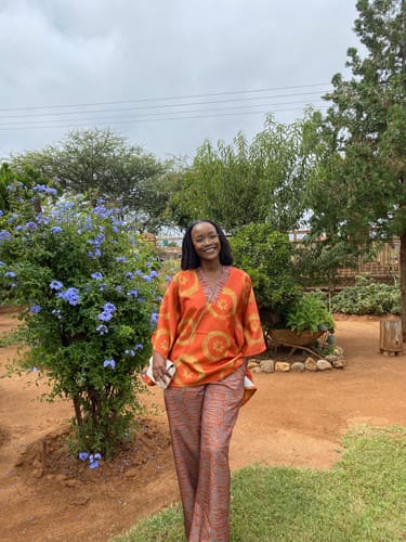 Reviewer smiling in a garden wearing the orange patterned Loose Top & Wide-Leg Pants set.