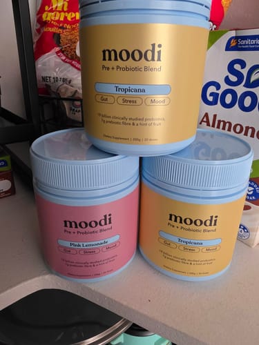 Customer's three tubs of moodi Pre + Probiotic Blend, two Tropicana and one Pink Lemonade, stacked on a counter.