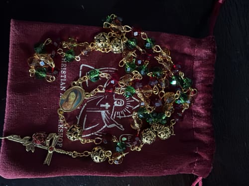Reviewer's vintage Christmas rosary with red and green faceted beads, displayed on its dark red velvet pouch.