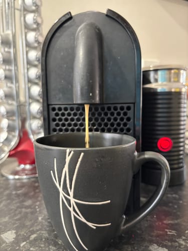 Customer brewing Blend 9 coffee from a Nespresso machine into a dark patterned mug.