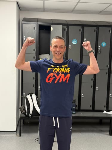 Reviewer smiling and flexing in a gym locker room while wearing the Go To The F*cking Gym T-Shirt.