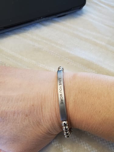 Customer's wrist wearing the LOVE YOU MORE bracelet, showing the engraved message on the stainless steel bar.