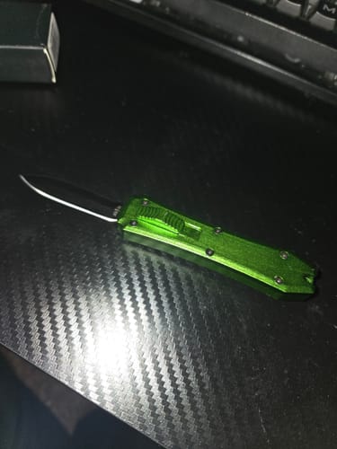 Customer's green Micro OTF knife shown with the blade extended on a textured black tabletop.