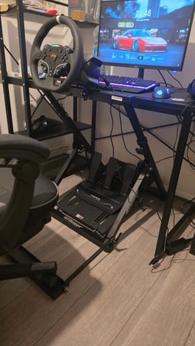 Customer's black APEX Wheel Stand with a racing wheel and pedals set up in front of a desk and monitor.