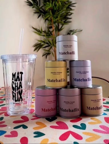 Un cliente muestra seis latas de diferentes colores del Pack Sabores de Té Matcha apiladas sobre una mesa junto a un vaso de la marca.