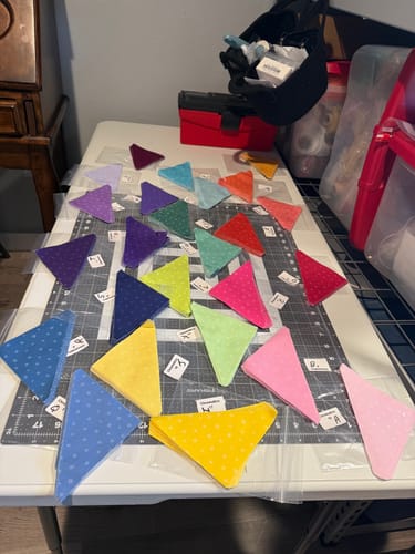 Customer's colorful, pre-cut fabric triangles from the Color Study Quilt Kit laid out on a work table.