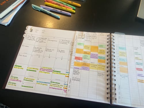 Reviewer's open Rose Planner showing a color-coded monthly view and weekly time-blocking pages on a desk.