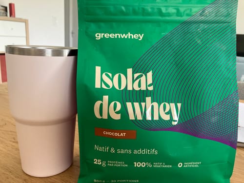 Sachet de l'Isolat de Whey Native d'un client, saveur chocolat, posé sur une table à côté d'un gobelet.