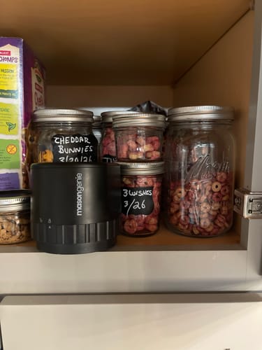 Customer's black Mason Genie vacuum sealer on a pantry shelf next to several sealed jars of food.