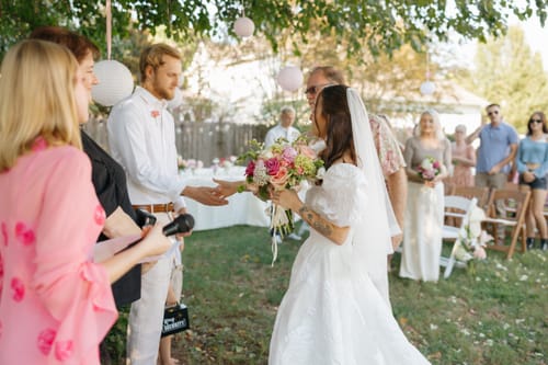 Customer at her outdoor wedding ceremony wearing the simple, elbow-length TOMMIE VEIL with her dress.