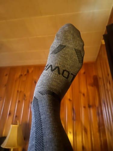Reviewer raises their foot to show the sole and heel of the grey Men's Alpaca Sock.