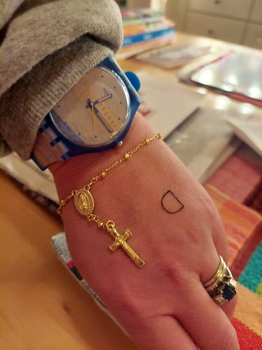 Customer's wrist wearing the gold-colored Rosario Bling Lupita Bracelet, styled with a watch and rings.