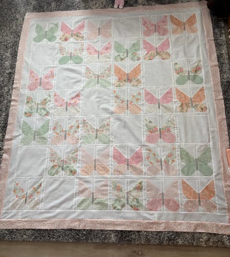 Customer's completed Winging It quilt top laid out, showing the beautiful butterfly design made with pastel floral fabrics.