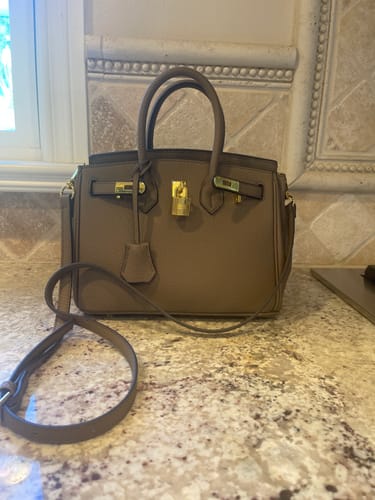 Customer's taupe LALUVA Warkin Bag with gold hardware and a shoulder strap, placed on a countertop.
