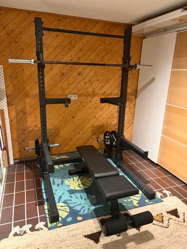 Kunde zeigt das montierte R7 Squat Rack mit Hantelbank und Langhantel in einem Raum.