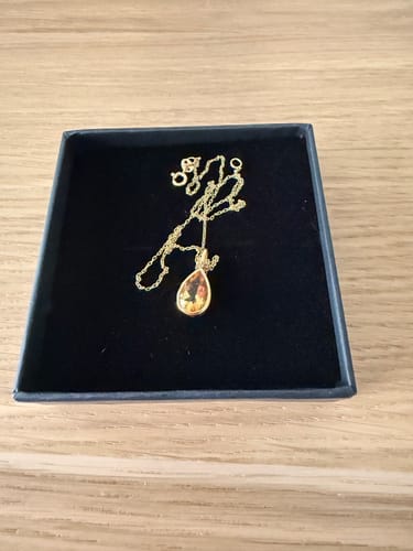 Le Pendentif Citrine d'un client avec sa pierre claire, posé dans son écrin noir sur une table en bois.
