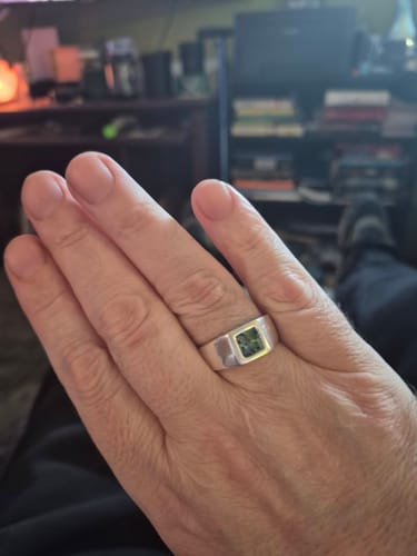 A customer's hand wearing the Men's Opal Ring. The sterling silver ring features a dark, mottled opal in a square bezel.