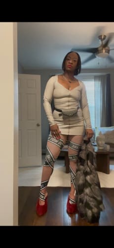 Reviewer standing in a room wearing the LEATHER ENERGY MINI DRESS with statement leggings and red heels.