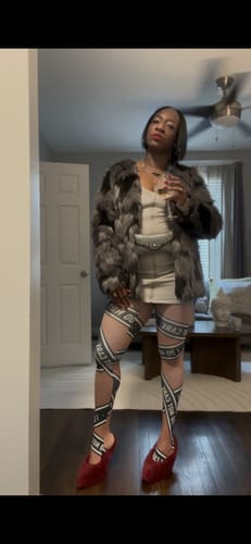 Reviewer wearing the LEATHER ENERGY MINI DRESS under an open furry coat, styled with red heels.