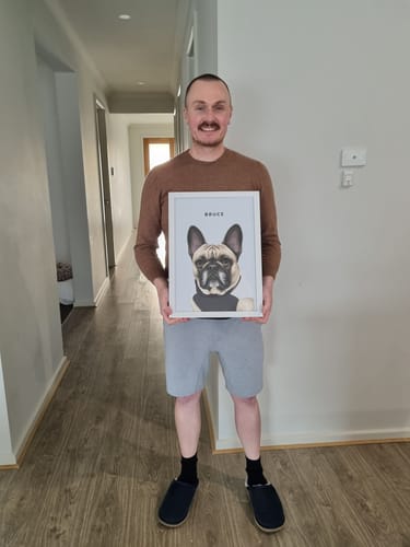 Customer holding a white-framed Custom Pet Portrait of a French Bulldog named Bruce in a hallway.