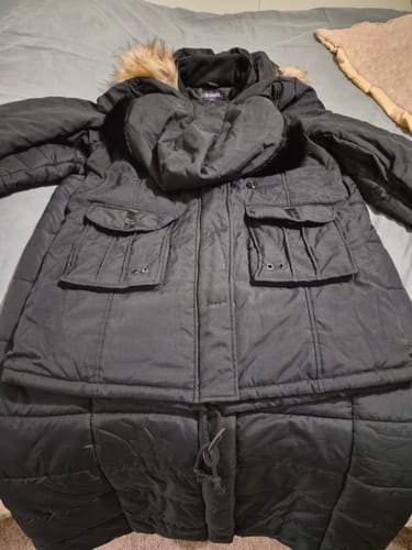 Customer's black hooded parka with faux fur trim laid flat on a bed, showing the pockets and drawstring waist.