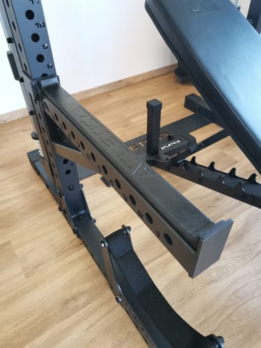 Ein Kunde zeigt die schwarzen, stabilen R7 Spotter Arms, die an einem Power-Rack montiert sind.