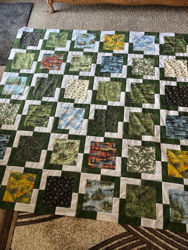 Customer's completed Iconic Quilt top spread on the floor, showing its grid of outdoorsy-print squares with green and white sashing.
