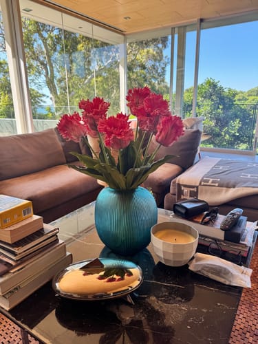 Customer's vibrant Pink Parrot Tulips with ruffled edges in a blue vase on a coffee table.
