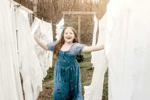 Customer happily posing outdoors in the dusty blue Crinkled Chiffon Dress and a matching hair bow.