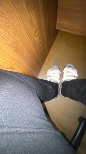 A customer's point-of-view of their feet in the bright, reflective Storm Dracos V2 slides indoors.