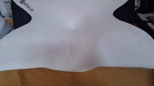 Client montrant le coussin d'alignement cervical Cellsius, blanc et ergonomique, posé sur un lit.
