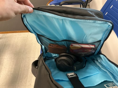Cliente mostrando el espacioso interior celeste de la Mochila X Pack con auriculares y objetos dentro de los bolsillos de malla.