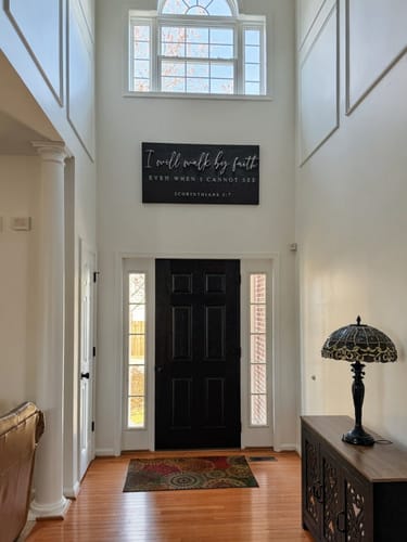 Reviewer's black faith sign hanging above the front door in a bright entryway with high ceilings.