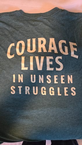 Customer's close-up of the back of the green "Unseen Struggles" tee, showing the 'Courage Lives In Unseen Struggles' print.