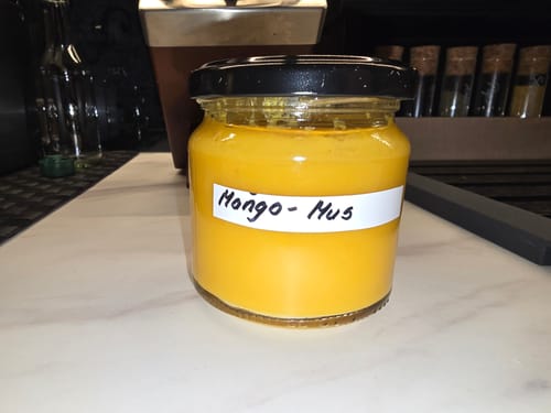 Ein Kunde zeigt ein Glas mit leuchtendem Mango-Mus, das aus den Mangos der Mix-Box hergestellt wurde.