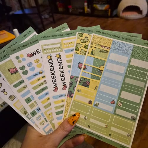 Reviewer's hand holding several cute 'Cute Critters' sticker sheets from the Ultimate Subscription.