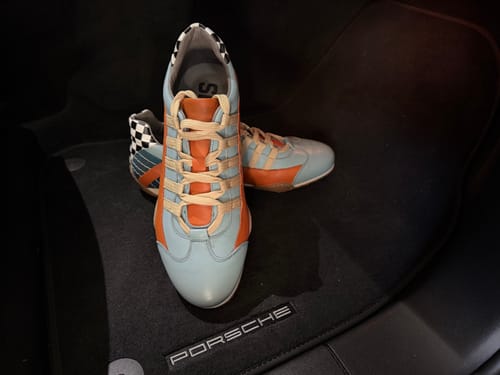 Customer's blue and orange Men's Racing Sneakers placed on a dark car floor mat.