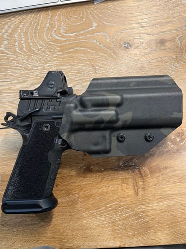 Reviewer's black camouflage OPTIO V2 holster holding a handgun with a red dot sight on a wooden surface.