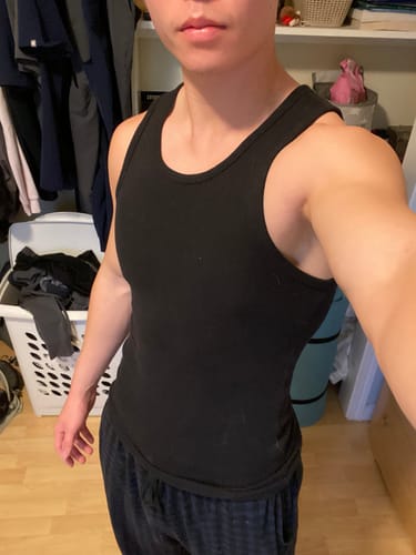 Customer wearing the close-fitting black Cotton Fitted Tank in a bedroom.