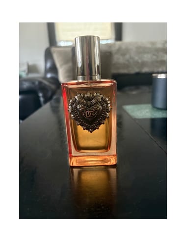 Reviewer's bottle of Devotion Intense perfume, showing its amber liquid and ornate heart emblem, sitting on a table.