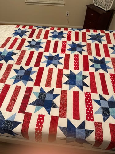 Reviewer's large 'Red, White, and Cute' quilt top spread across a bed during assembly, showing the star and stripe pattern.