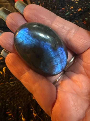 Reviewer holding the smooth, dark crystal in their hand, showing its beautiful blue flash.
