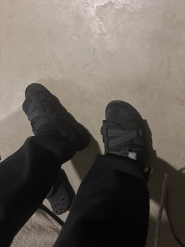A customer's top-down view of the black Reflective DracoSlides paired with black trousers indoors.
